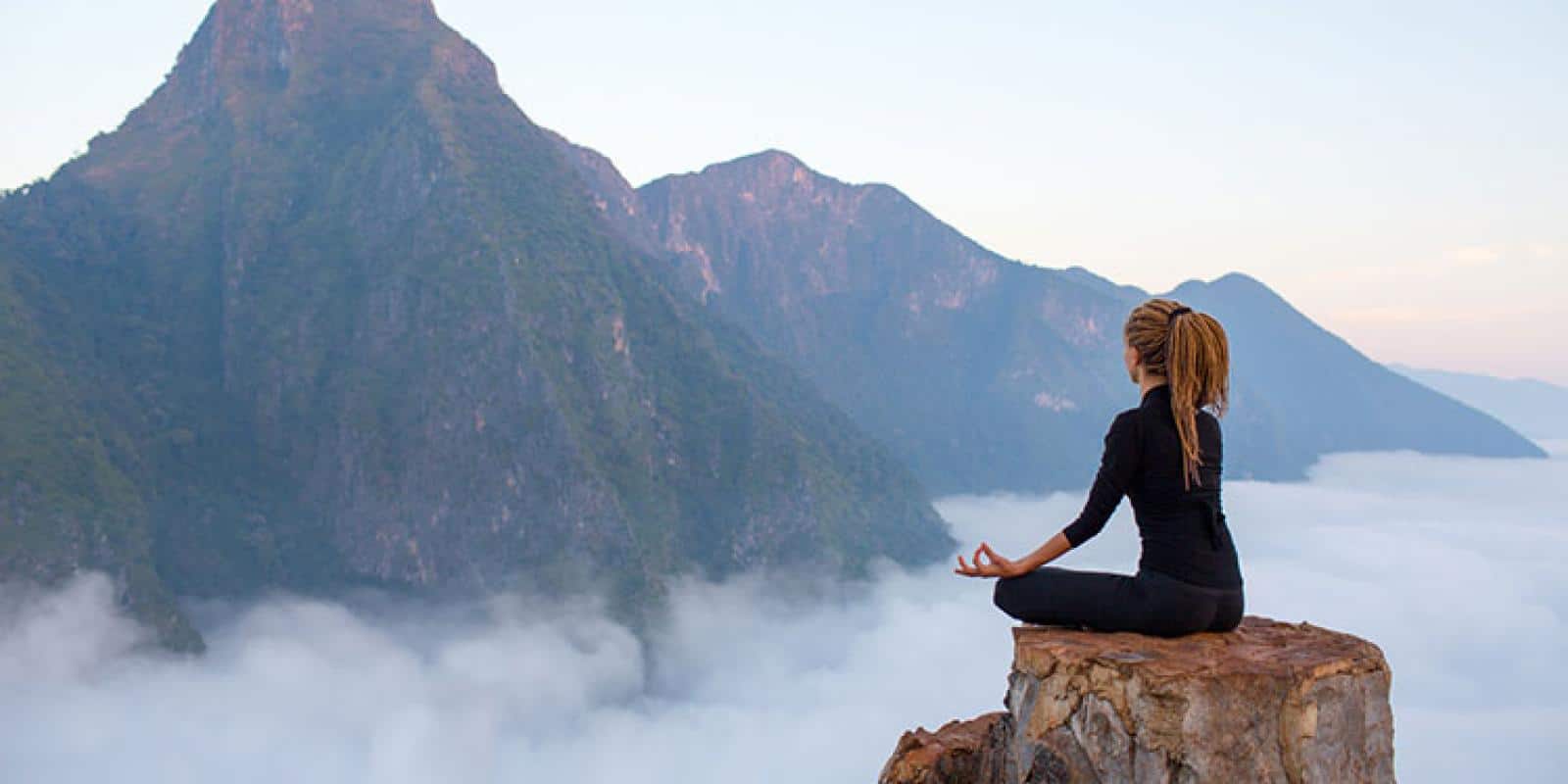 Frau meditiert zum Sommenaufgang auf einem Berg.