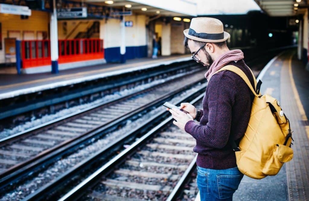 Mann steht am Bahnsteig mit Smartphone in der Hand