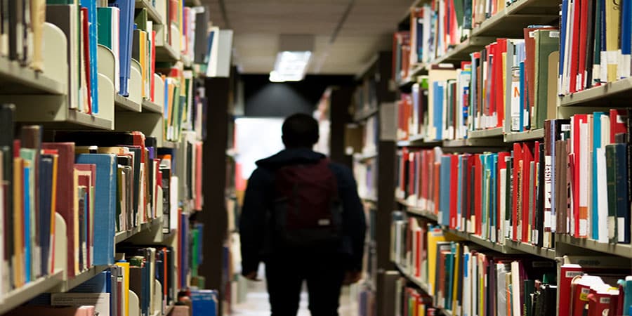 Person von Hinten im Gang einer Bibliothek - Symbolbild für "Studenten-Apps"