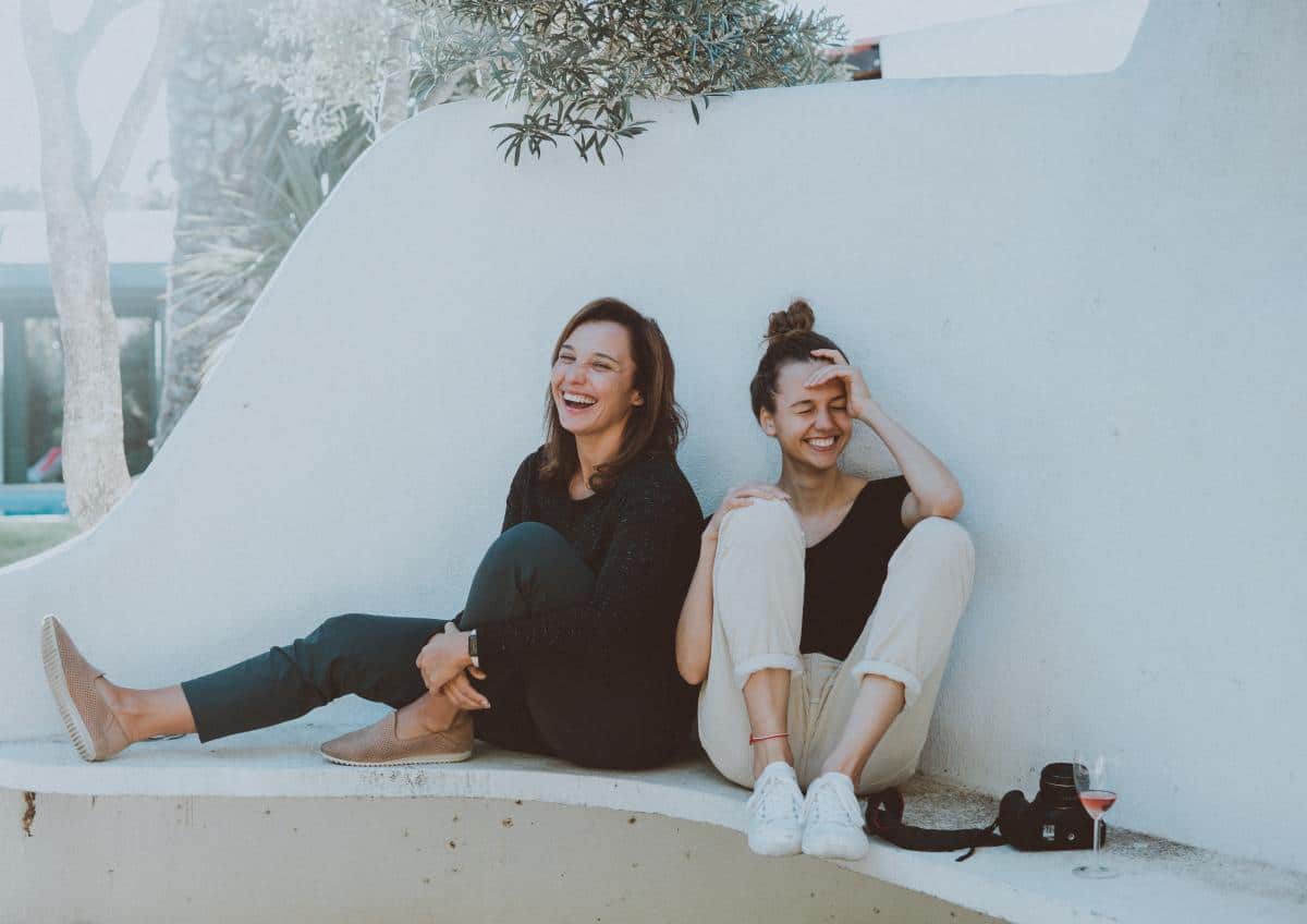 Zwei Frauen sitzen draußen in der Sonne und lachen zusammen