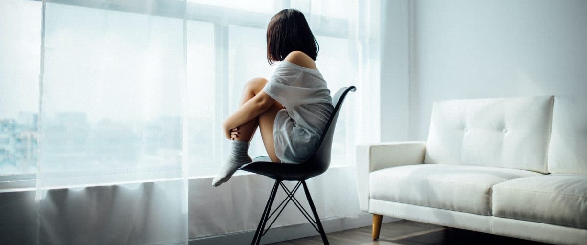 Frau sitz mit angewinkelten Beinen auf einem schwarzen Stuhl in einem weiß eingerichteten Zimmer