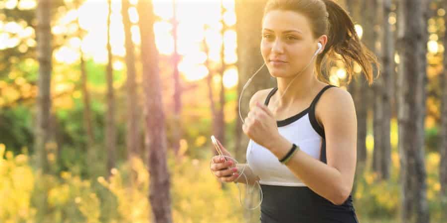 Frau joggt durch den Wald mit Smartphone in der Hand und Kopfhörern in den Ohren