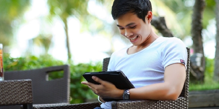 Junger Mann schaut lächelnd auf ein Tablet - Symbolbild im Beitrag zu Apps für Studenten
