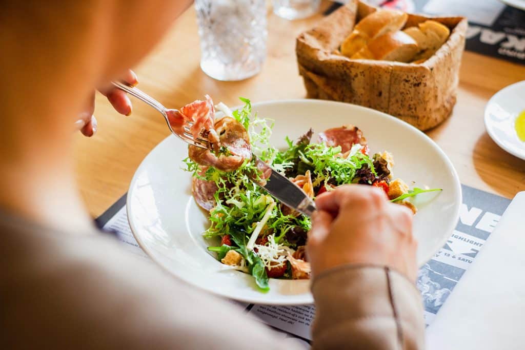 Eine Person, die am Essenstisch einen Salat isst - Symbolbild für ausgewogene Ernährung im Studienalltag.