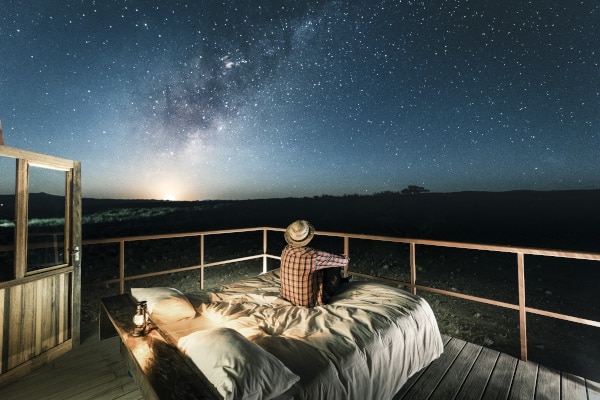 Tourist sitzt auf einem Bett draußen und bewundert die Sterne.