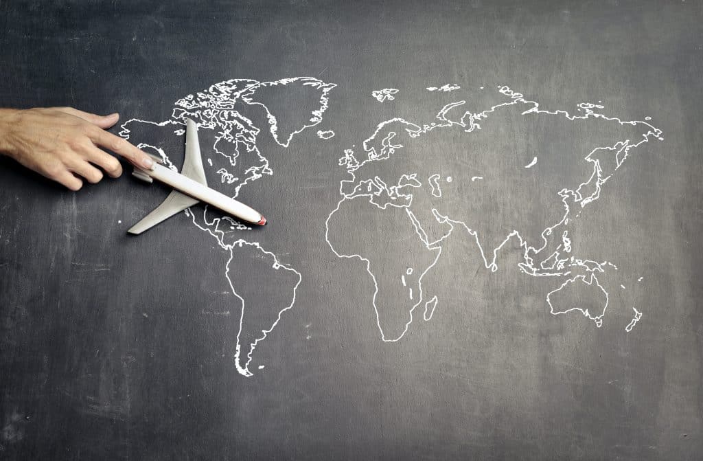 Mit Kreide auf eine Tafel gemalte Weltkarte, auf der eine Hand ein Miniaturflugzeug bewegt - Symbolbild für Auslandssemester