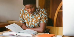 Studentin sitzt an Schreibtisch mit Buch vor sich und liest - Symbolbild für Master