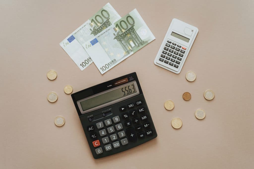 Taschenrechner auf einem Tisch, umgeben von Geldscheinen und Münzgeld - Symbolbild für Finanzen