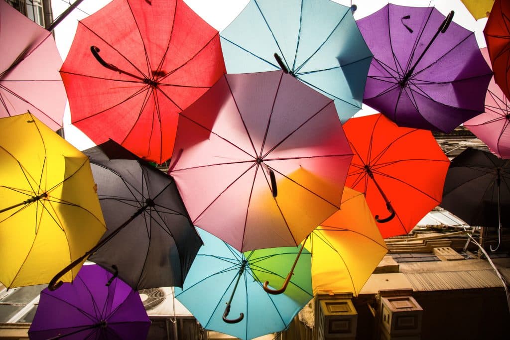 Bunte, aufgespannte Regenschirme über einer Straße - Symbolbild für Versicherung