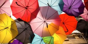 Bunte, aufgespannte Regenschirme über einer Straße - Symbolbild für Versicherung
