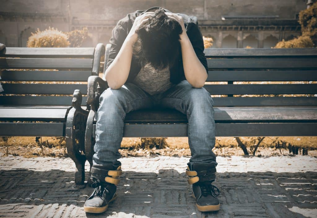 Junger Mann sitzt auf Parkbank und hat vor Verzweiflung den Kopf auf den Knien - Symbolbild für Probleme im Studium