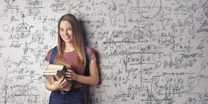 Junge Frau mit Büchern in der Hand steht vor einer Wand voller Formeln - Symbolbild zum Studienbeginn