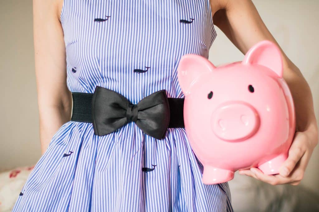Junge Frau im blauen Kleid hält ein großes Sparschwein unter dem Arm - Symbolbild für Sparen im Alltag