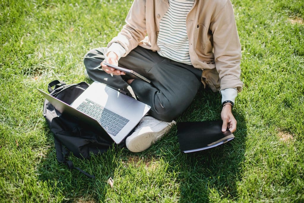 Junge Frau sitzt mit Laptop im Gras - Symbolbild für Bewerbung um einen Studienplatz