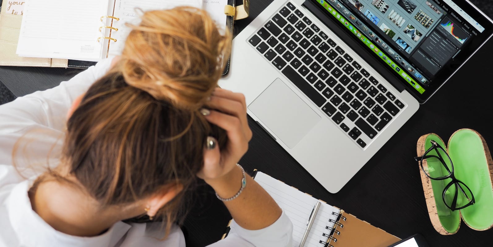 Eine junge Frau sitzt vor ihrem Laptop mit dem Kopf in ihren Händen - Symbolbild für Stress im Studium.