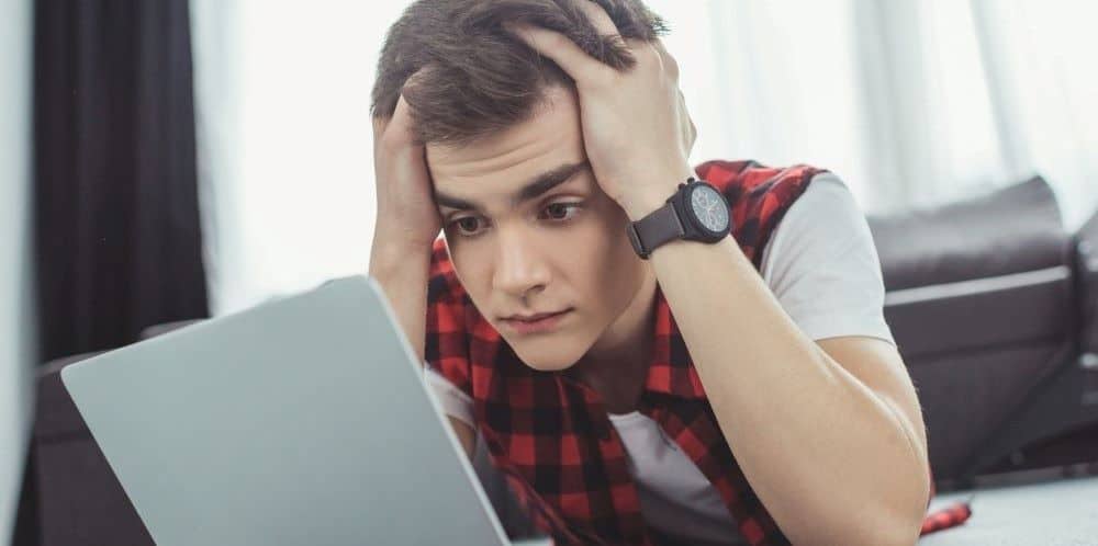 Ein Student sitzt vor einem Laptop, den Kopf in die Hände gestützt, und schaut fragend - Symbolbild für das ISIC Kontaktformular